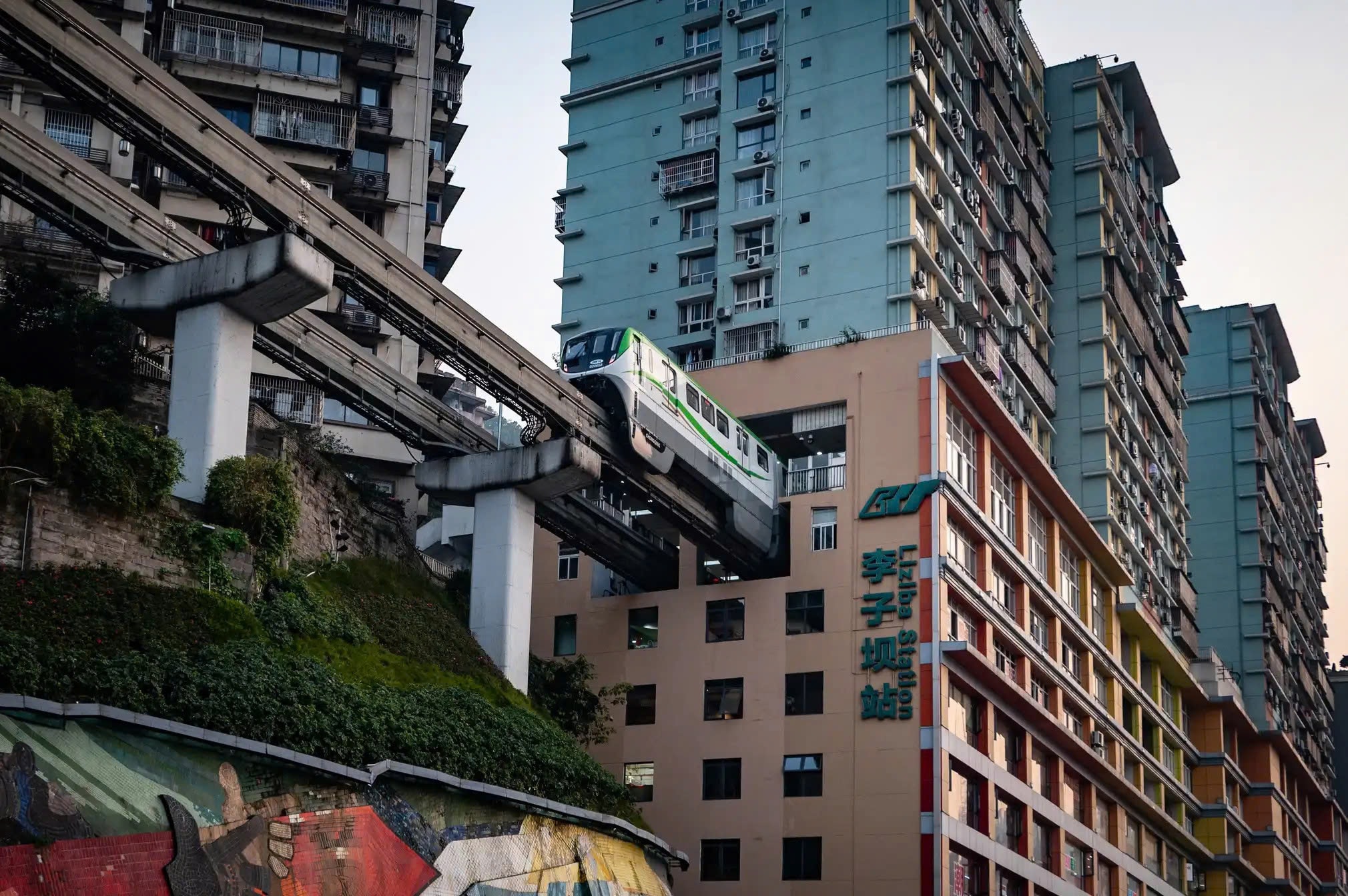 Từ lâu Trung Khánh đã được mệnh danh là “thành phố núi” bởi phần lớn diện tích nằm trên địa hình đồi dốc. Chính đặc thù này khiến hạ tầng đô thị được xây dựng men theo các triền núi, hình thành nên mạng lưới giao thông chằng chịt, phức tạp chẳng khác nào mê cung. Trong hình là tàu điện ngầm số 2 đi xuyên qua chung cư 19 tầng ở Trùng Khánh.