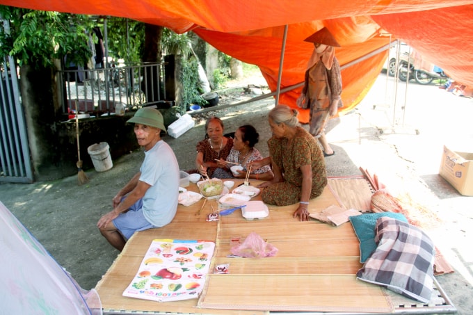 Bà Chung (ngồi trên ván) và bà Thơm (bên cạnh) ăn cơm từ thiện dưới chiếc bạt, trên đê Đô Tân, xã Trung Giã trưa 12/10. Ảnh: Phan Dương