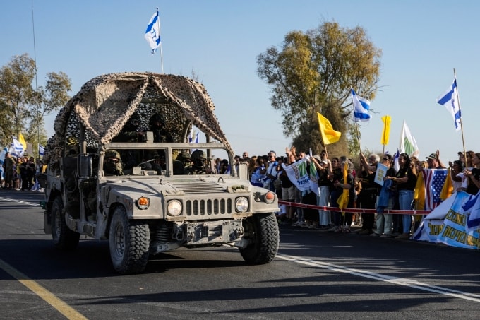 Xe quân sự chạy qua nhóm người Israel mang theo quốc kỳ để chào đón con tin trở về bên ngoài căn cứ quân sự Reim, gần biên giới Gaza ở miền nam Israel, ngày 13/10. Ảnh: AFP