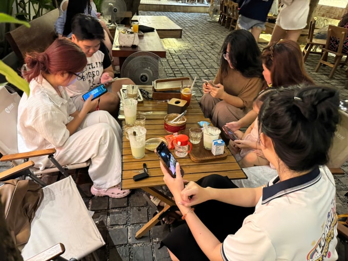 Hồng Nhung (búi tóc), 26 tuổi, ở phường Cầu Giấy, Hà Nội cặm cụi chơi điện thoại trong một buổi cà phê, tháng 10/2025. Ảnh: N.T
