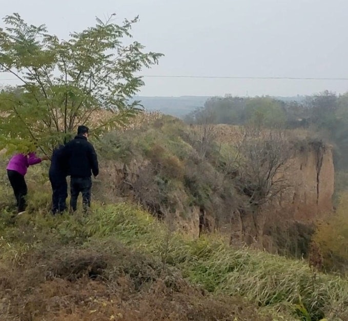 Gia đình đứng bên vực, nhìn xuống nơi Lan bị chồng ném xuống. Nạn nhân được cơ quan chức năng dùng dây thừng kéo lên nhưng đã tử vong. Ảnh: Shangyou