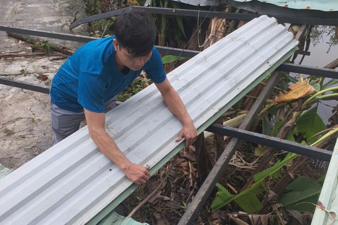 Người dân thu gom mái tôn bị lốc xoáy làm hư hại. Ảnh: Thân Trường