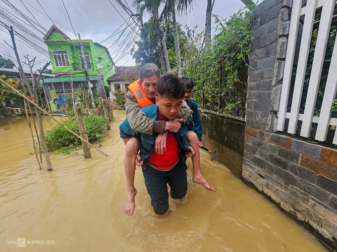Lực lượng dân quân tự vệ phường Tây Nha Trang cõng người già từ vùng ngập đến điểm tránh trú an toàn. Ảnh: Bùi Toàn