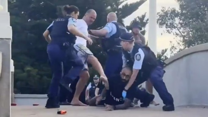 Cảnh sát Australia cố tách đám đông giận dữ khỏi người bị nhận diện nhầm là nghi phạm xả súng ở bãi biển Bondi. Ảnh: 7News