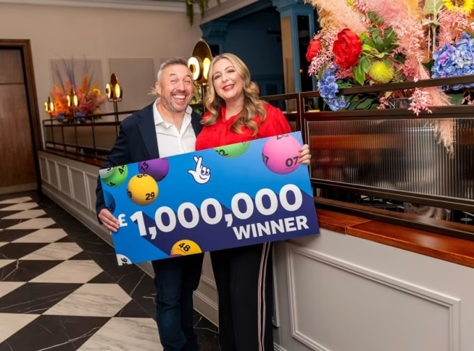 Đôi vợ chồng người Anh Richard Davie và Faye Stevenson-Davies chụp ảnh bên tấm biển kỷ niệm người trúng giải độc đắc 1 triệu bảng Anh hôm 16/12. Ảnh: CNN