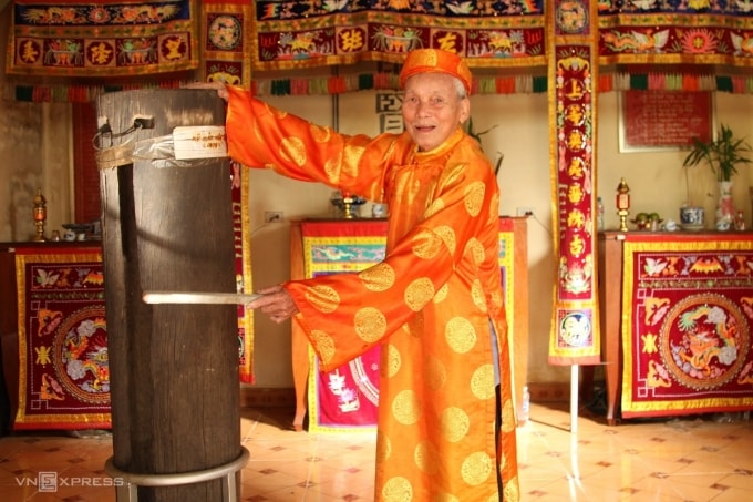 Ông Quách Vĩnh Kinh gõ vào chiếc mõ gỗ sến đỏ trong đình làng Trung Lương. Ảnh: Thảo Vy