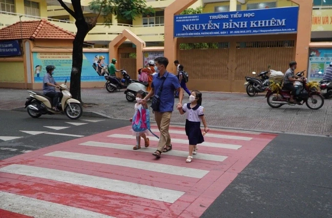 Phụ huynh dắt con qua đường Nguyễn Bỉnh Khiêm, quận 1 cũ, trước trường tiểu học được sơn màu nâu đỏ kết hợp với màu trắng. Ảnh: Giang Anh