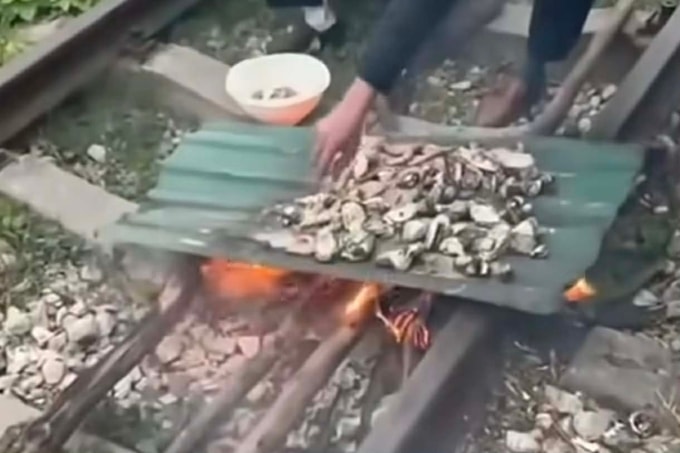 Hai người đốt lửa nướng đồ ăn trên đường sắt. Hình cắt từ video.
