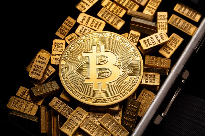 Đồng xu biểu trưng Bitcoin được đặt trong két sắt chứa những thỏi vàng 100g. Ảnh: CNBC