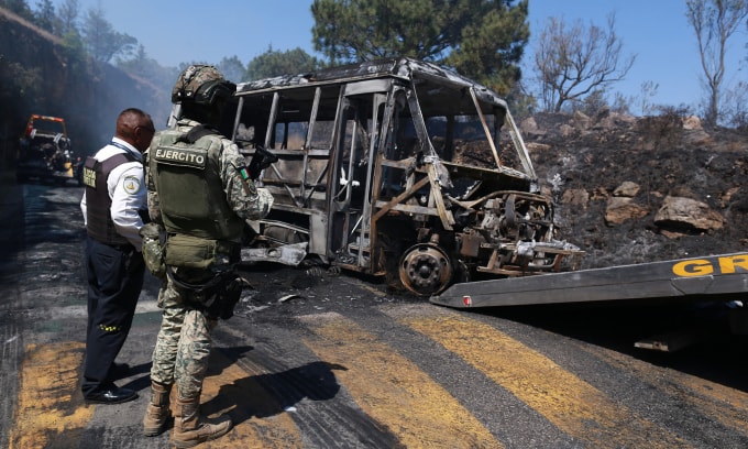 Pedestrians walk past a charred vehicle after it was set on fire, on a road in Cointzio, Michoacán state, Mexico, Sunday, Feb. 22, 2026, after the death of the leader of the Jalisco New Generation Cartel, Nemesio Rubén Oseguera Cervantes, known as El Mencho. (AP Photo/Armando Solis)