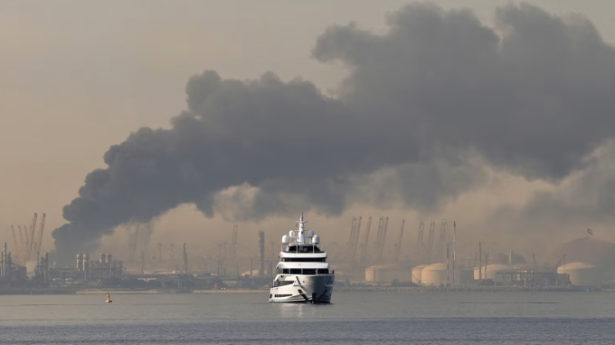 Một du thuyền đi ngang qua cột khói bốc lên từ cảng Jebel Ali Port sau cuộc tấn công được cho là của Iran nhằm vào Dubai ngày 1/3. Ảnh: AFP