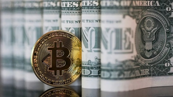 Biểu trưng của Bitcoin được đặt giữa các tờ đôla Mỹ. Ảnh: CNBC