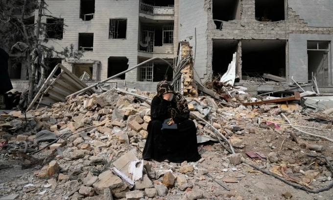 Người phụ nữ ngồi trên đống đổ nát đối diện một tòa nhà dân cư bị hư hại trong chiến dịch không kích của Mỹ và Israel tại thủ đô Tehran, Iran, hôm 12/3. Ảnh: AP