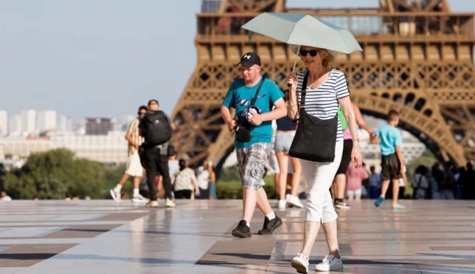 Du khách dùng ô để tránh nắng nóng khi đến thăm tháp Eiffel, Paris (Pháp) ngày 30/6/2025. Ảnh: AFP