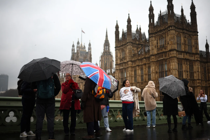 Du khách cầm ô khi đi bộ qua cầu Westminster ở London, phía trước tòa nhà Quốc hội. Ảnh: AFP