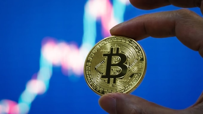 Nhà đầu tư đang cầm biểu trưng Bitcoin trước màn hình theo dõi thị giá. Ảnh: CNBC