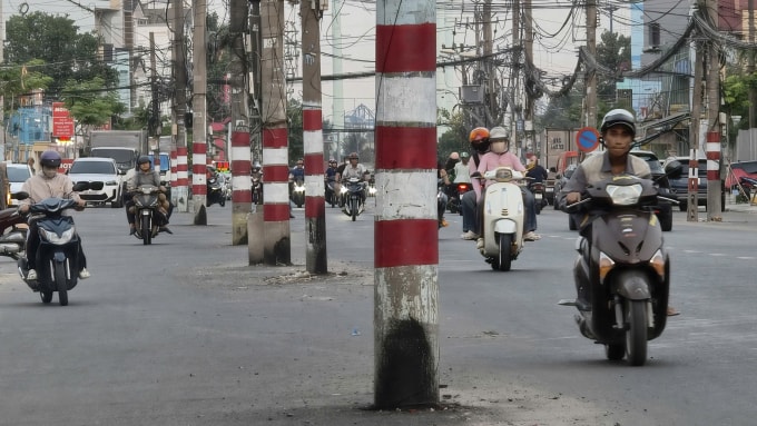 Người lái xe máy chạy bên cạnh hàng loạt tru điện nằm giữa đường Nguyễn Thị Định, phường Cát Lái sau mở rộng. Ảnh: Đình Văn